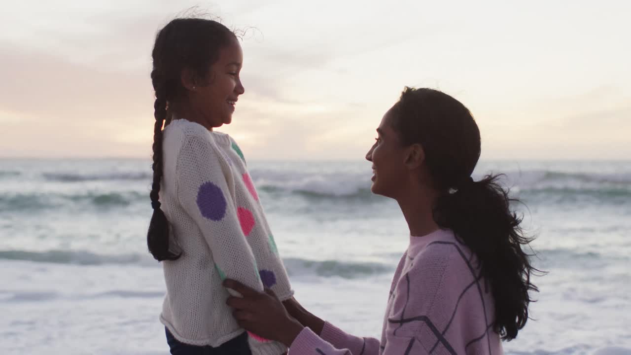 madre e hija hispanas felices en la playa al atardecer