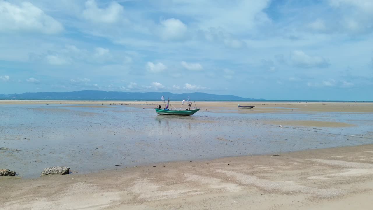 Drone video shows traditional small fishing boats anchored near the sandy shoreline of Koh Phangan, Thailand, with clear turquoise water and lush green coastline creating a scenic tropical seascape