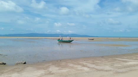 drone video shows traditional small fishing boats anchored near the sandy shoreline of koh phangan, thailand, with clear turquoise water and lush green coastline creating a scenic tropical seascape