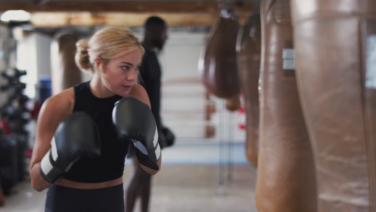 Female Boxer In Gym Training With Old Fashioned Leather Punch Bag