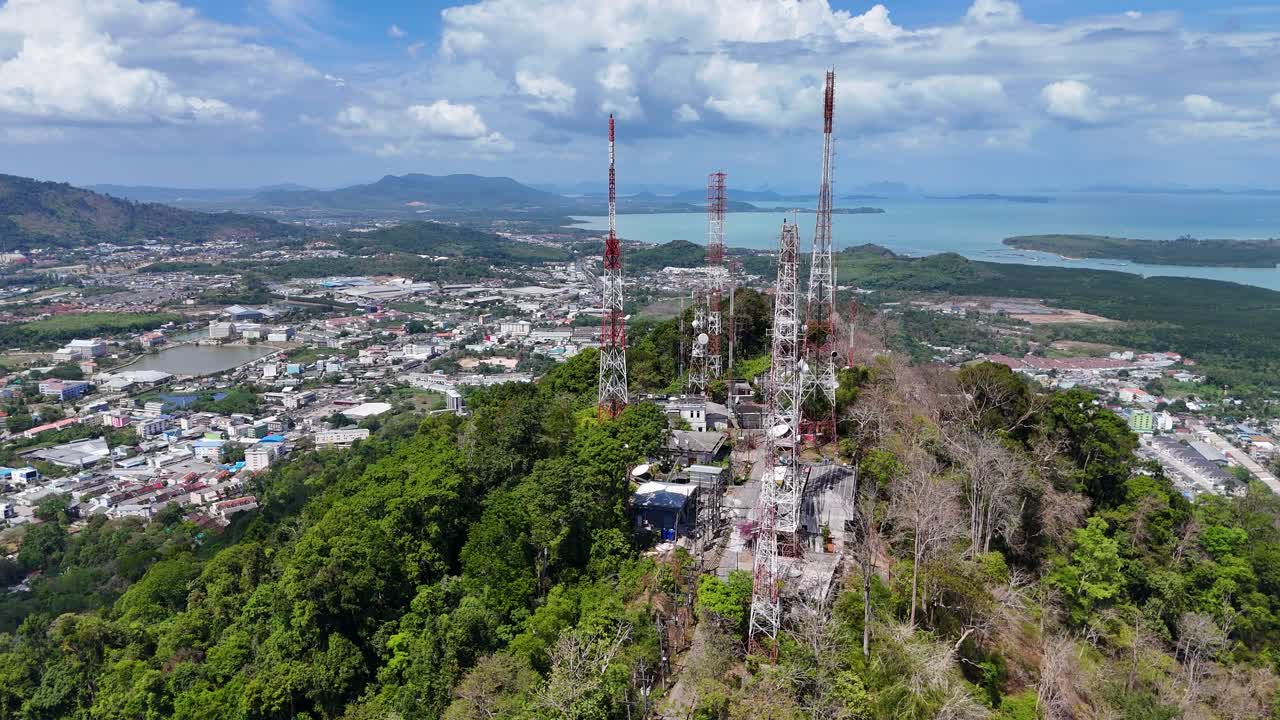 드론 영상은 푸켓의 원이 언덕에 있는 통신 타워를 포착합니다. 은 하늘 아래 푸른 초록색과 해안 풍경이 있습니다.