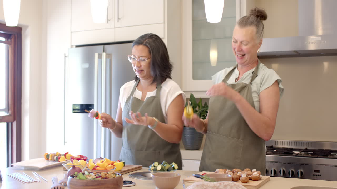 Senior diverse women preparing fresh vegetables in modern kitchen, enjoying cooking, at home