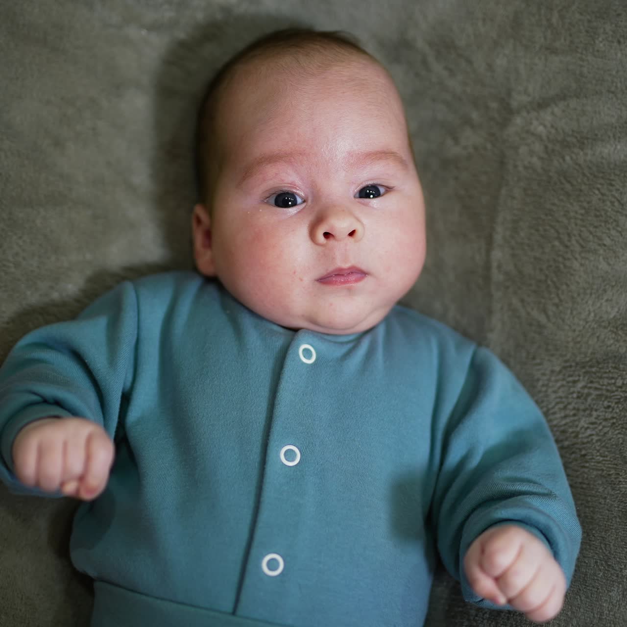 Little boy looks surprised staring into camera. Portrait of a beautiful child lying on bed close up. Grey backdrop
