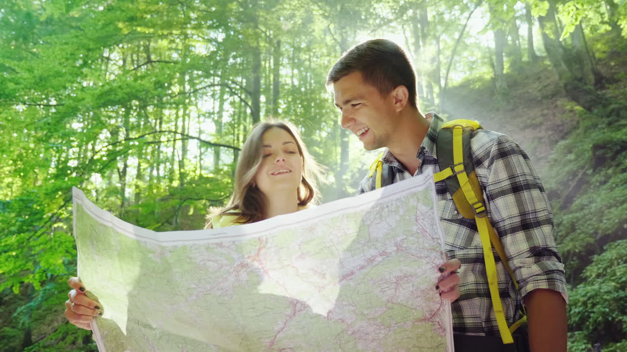 una pareja joven de turistas mirando un mapa se paran en los rayos del sol en el bosque cerca del