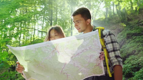 a young couple of tourists looking at a map they stand in the rays of the sun in the forest near the