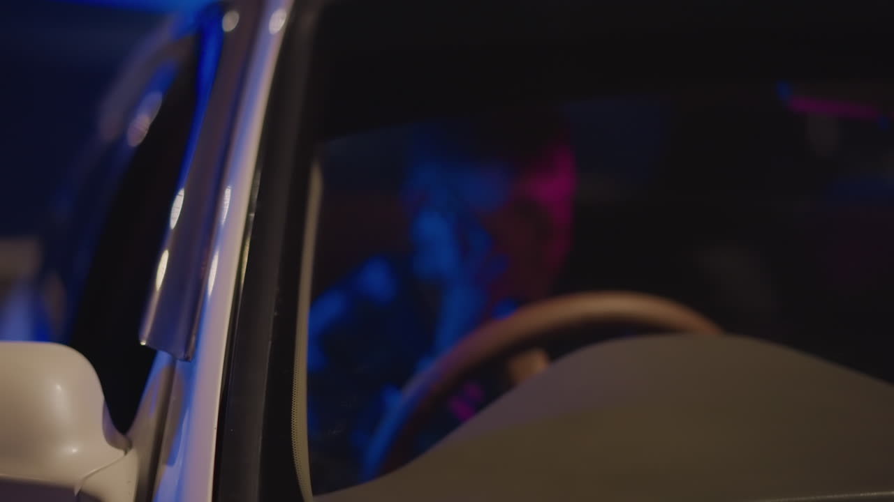 Coche aparcado de perfil lateral por la noche, conductor solitario hablando por teléfono con expresión reflexiva enmarcada por la ventana, carretera tranquila con bokeh y estelas de faros distantes, músico coordinando un ensayo tardío, noche