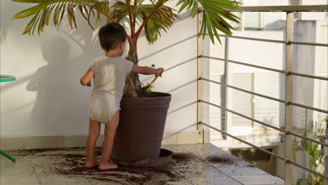 pequeño bebé latino sacando tierra de una maceta y dejándola caer al suelo con una cuchara de cocina de plástico verde