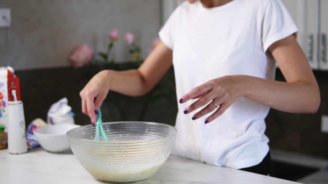 Unrecognizable woman prepares dough mixing ingredients in the the bowl using whisk. Homemade food. Slow Motion shot