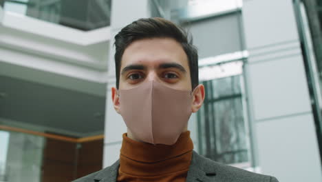 young businessman in mask posing for camera in office center