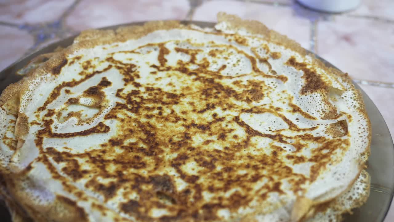 Una crêpe viene sollevata e girata con cura su una pila di pancake. La preparazione della colazione mostra una delizia semplice e gustosa.