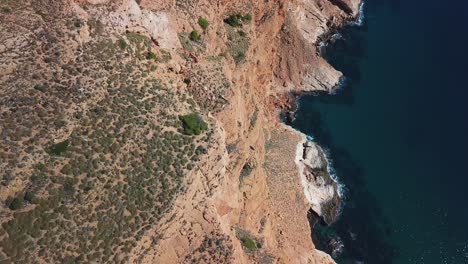 Establisher-slow-motion-shot-of-beautiful-cliff-and-terrain-of-a-mountain-with-small-trees-surrounded-by-ocean-on-all-sides-on-a-bright-sunny-day-in-Benidorm-city-in-Spain