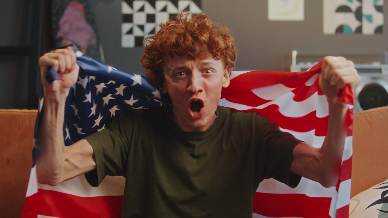 Excited Young Man Watching Sports on TV and Celebrating with USA Flag