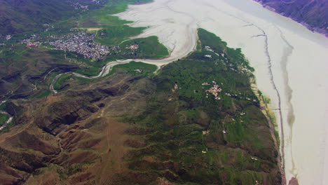 Top-Aerial-flight-view-over-the-village-surrounded-by-dry-river,-mountains-and-green-farms-and-trees,Forests-roads-and-streets-on-the-mountains