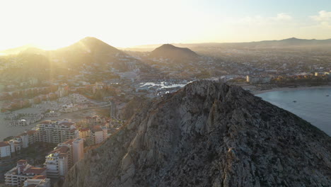 Tiro-De-Drone-De-Resorts-En-Playa-El-Médano-Con-Montañas-En-La-Distancia-Girando-Lentamente-Para-Revelar-La-Playa-Y-El-Océano-En-Cabo-San-Lucas-México,-Amplio