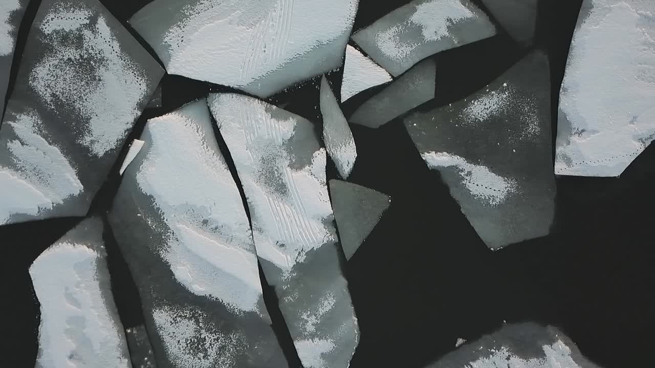 Drone shot flying over frozen lake covered in ice and snow flying sideways pass chunks of ice