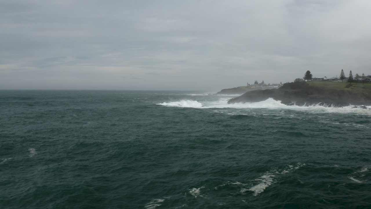Aerial pan of a rocky headland with large swell lines breaking on the rocks.