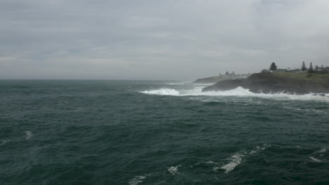aerial pan of a rocky headland with large swell lines breaking on the rocks.