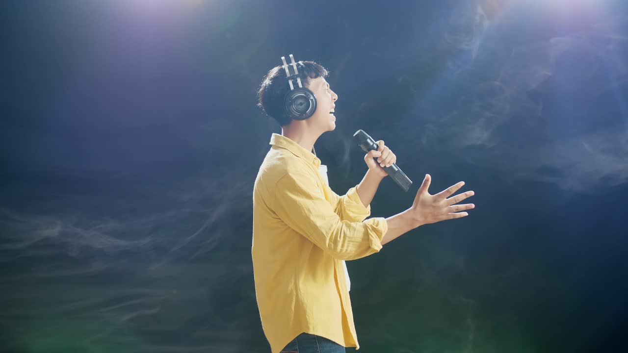 하 연기 검은 배경에 마이크를 들고 노래하는 젊은 아시아 소년의 측면 시각