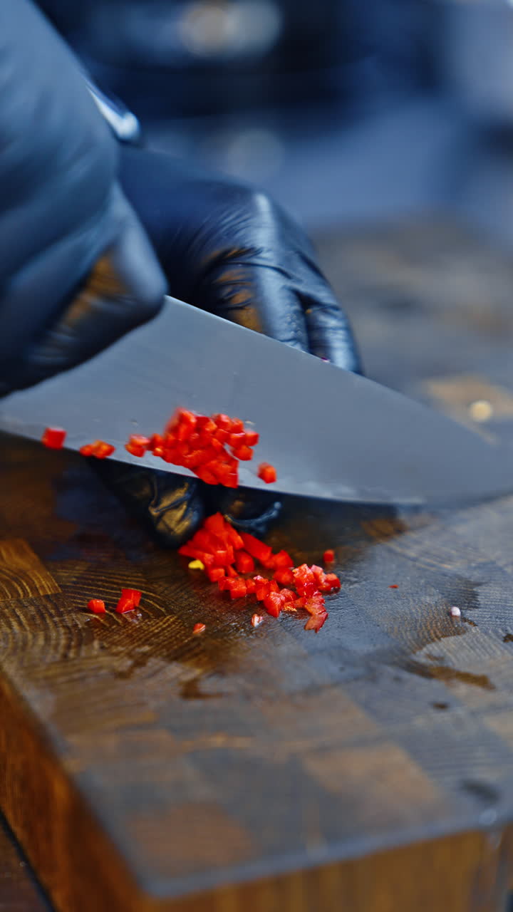 Hands of a chef in black gloves cut red pepper into little cubes. Using hot chili pepper in food. Close up. Vertical video.