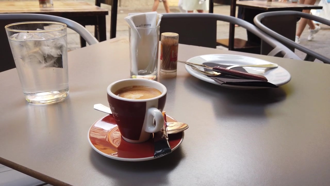 Primo piano di caffè espresso e acqua ghiacciata su un tavolo di un caffè all'aperto.