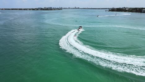 Die-Kamera-Bewegt-Sich-Im-Kreis-Um-Ein-Schnellboot,-Das-Ein-Schleppboot-In-Einem-Ozean-In-Der-Nähe-Eines-Strandes-Zieht