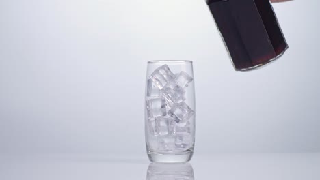 fresh cola being poured in to the glass with ice cubes on white background
