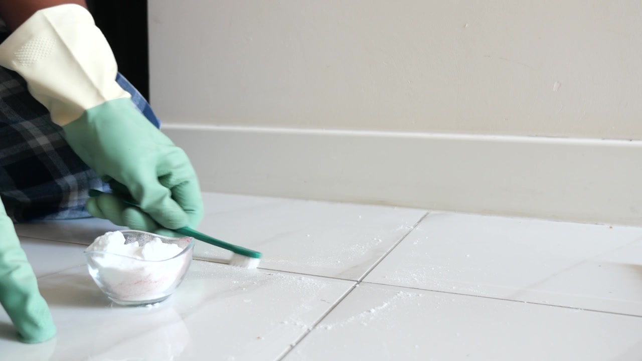 Person Cleaning Tile Grout with Toothbrush and Cleaning Powder