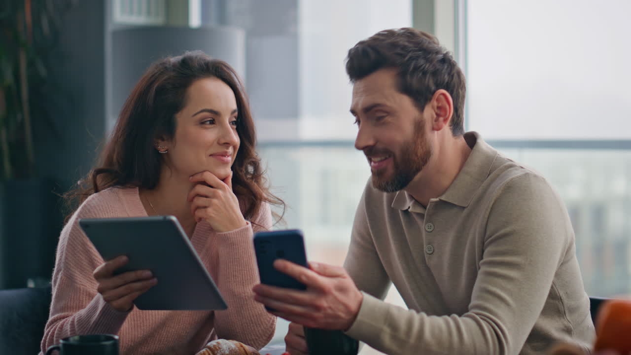 pareja alegre viendo aparatos divirtiéndose con las redes sociales en el primer plano de la cocina
