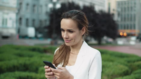 portrait of smiling female professional writing message on phone in city walk.