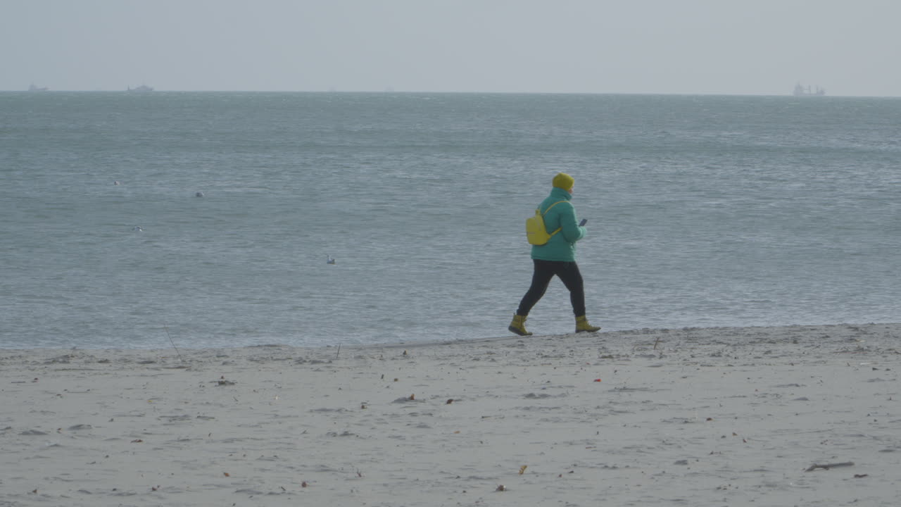 persona solitaria caminando a través de la tranquila playa de arena en una mañana nublada