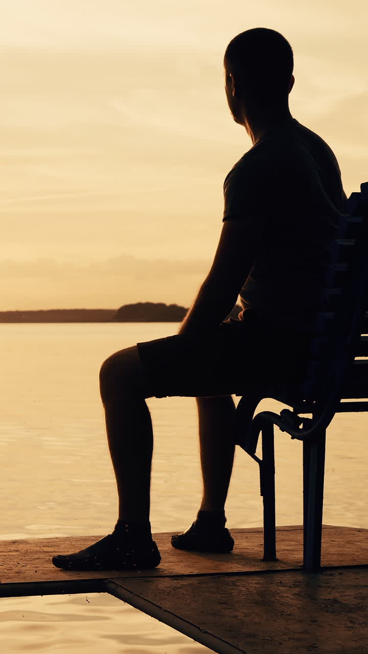 Peaceful sunset over a lake with a person sitting on a bench. Vertical video