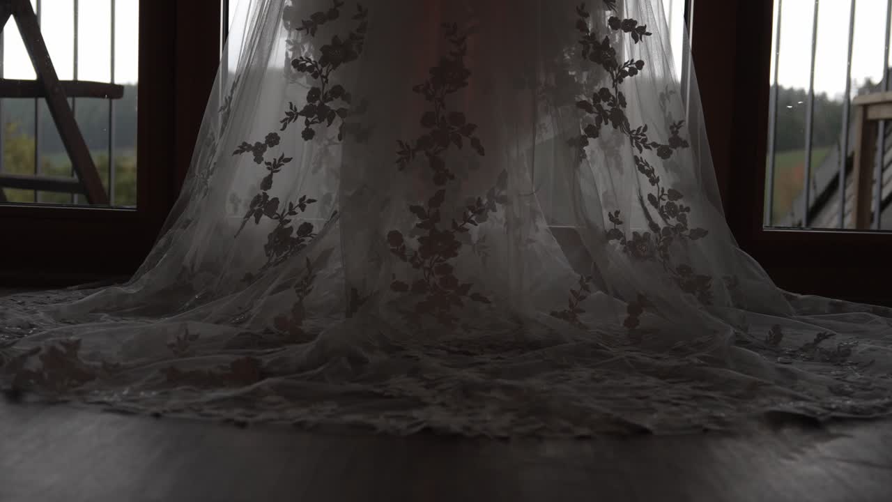 Close view of a wedding dress lace train lying on the floor with floral details illuminated by soft window light