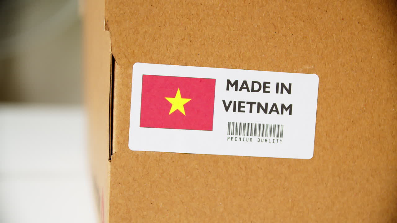 Hands applying MADE IN VIETNAM flag label on a shipping cardboard box with products