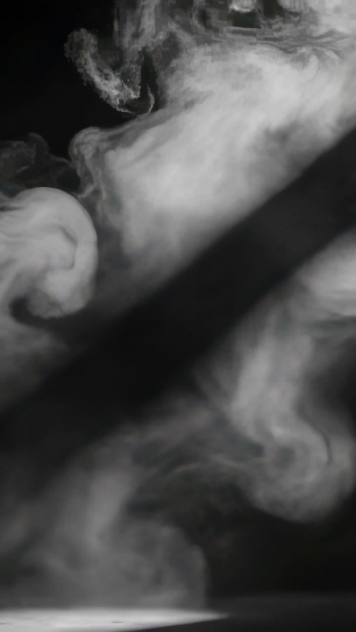 Video verticale: Fumo bianco che sale in studio dalla base, si arriccia in volute e si deforma per l'ombra.