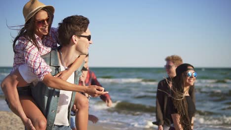 Paar-Hat-Spaß-Beim-Huckepackfahren-Zusammen-Mit-Einer-Jungen-Gruppe-Von-Menschen,-Die-Glücklich,-Fröhlich-Und-Verspielt-Lachen-Und-Die-Naturlandschaft-Am-Strand-Genießen.-Zeitlupenaufnahme