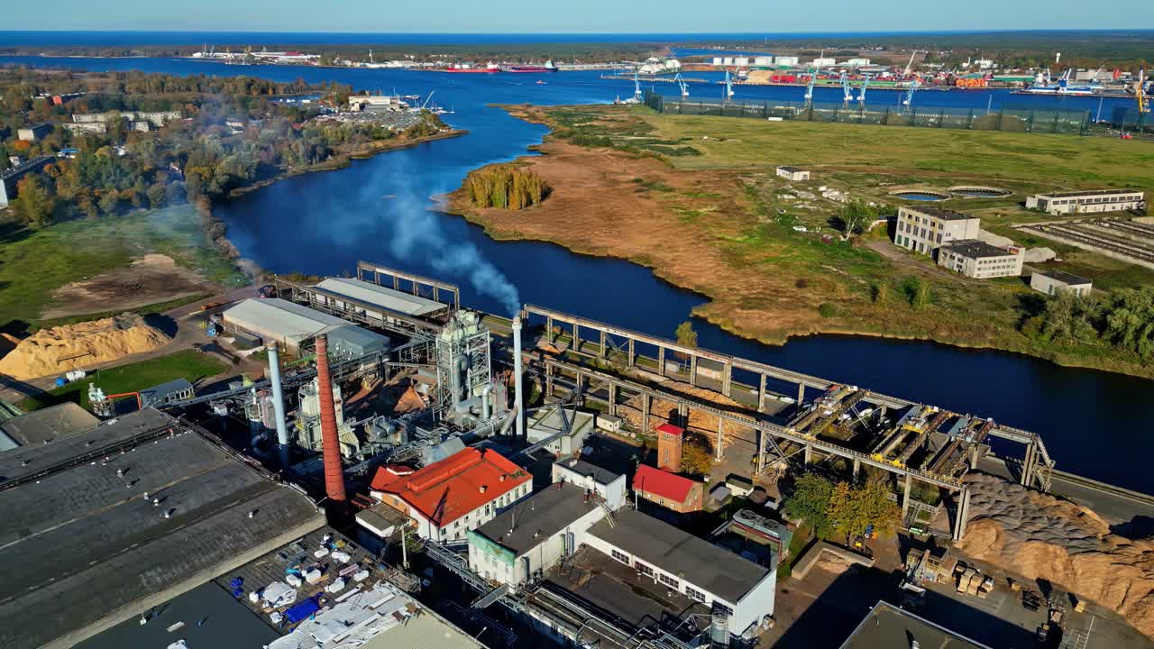 Luftfoto: Fabrik med Daugava-floden og Østersøen i Riga, Letland, om dagen, kredsende droneoptagelse
