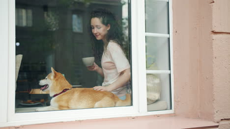 woman enjoying coffee with her dog by the window