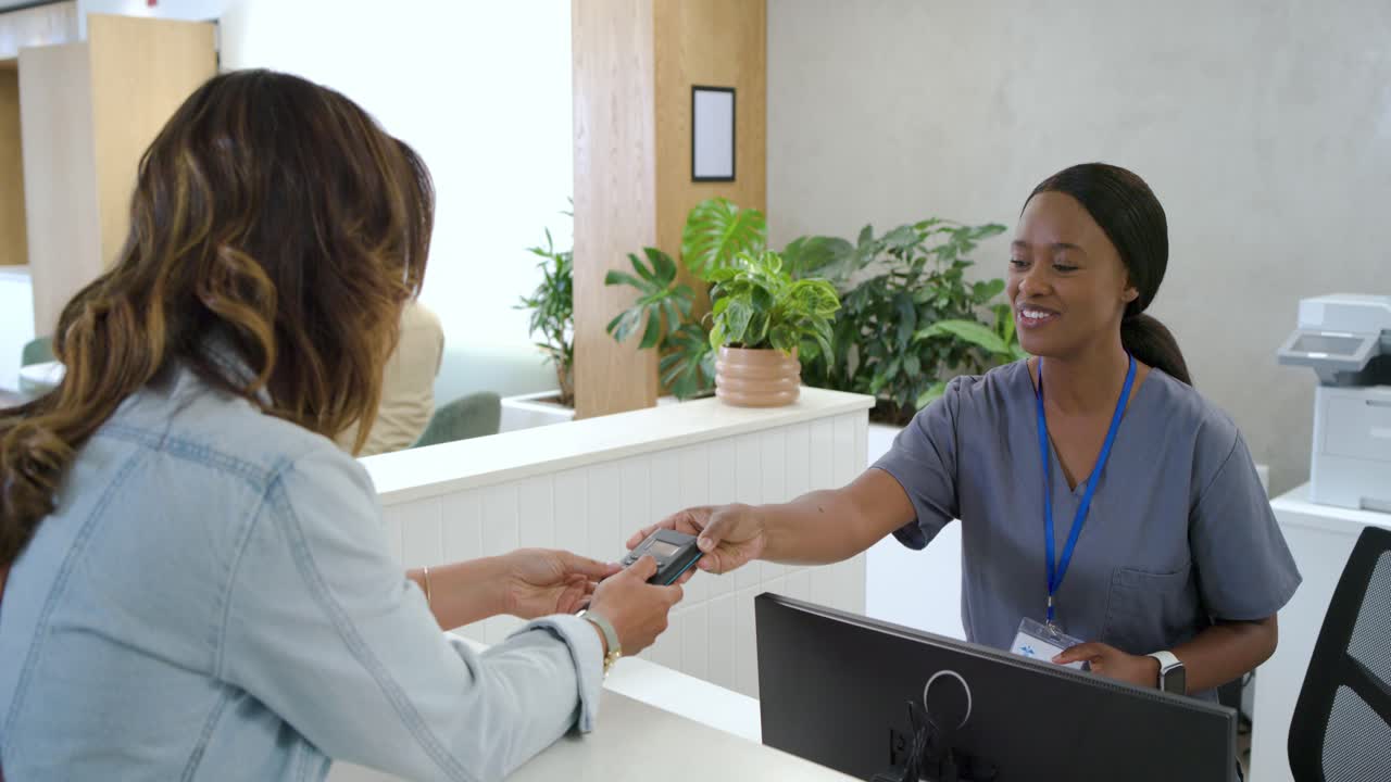 Recepcionista usando uniforme cirúrgico e visitante chegando pagando pela visita usando terminal na clínica