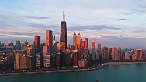 Drone-circling-the-sunlit-skyline-of-Chicago-skyline,-dramatic-sunrise-in-USA