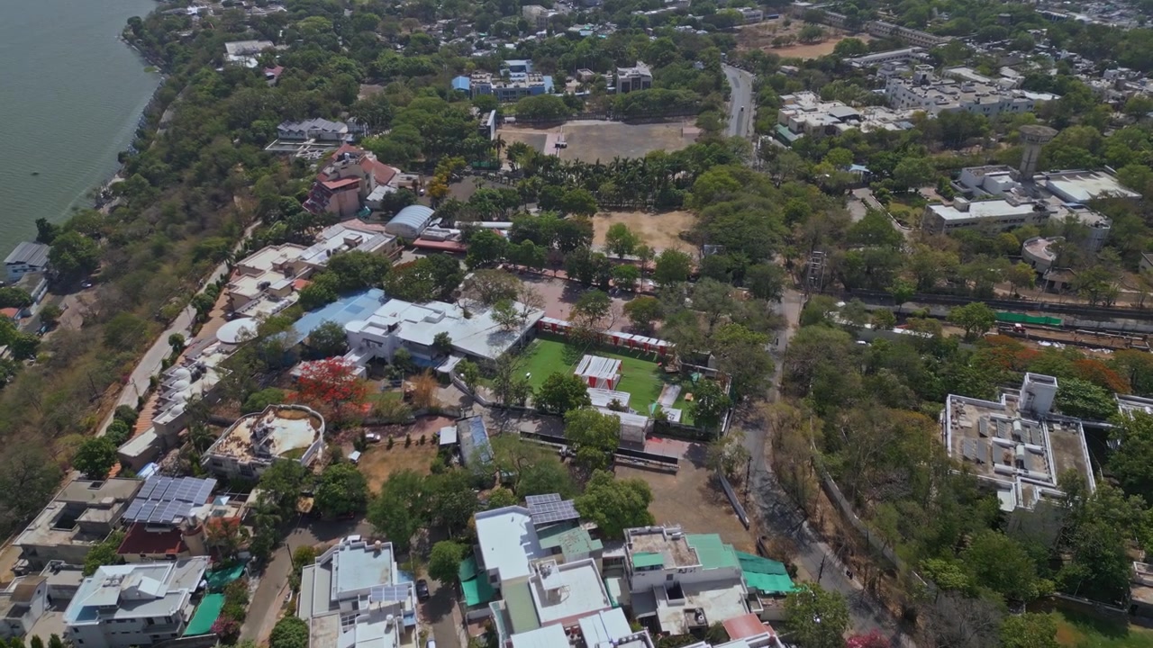 Rekaman drone terbang di atas lingkungan perumahan hijau dekat Danau Atas di Bhopal, menampilkan pembangunan perkotaan, tutupan pohon, jalan, dan lingkungan tepi danau dari atas.
