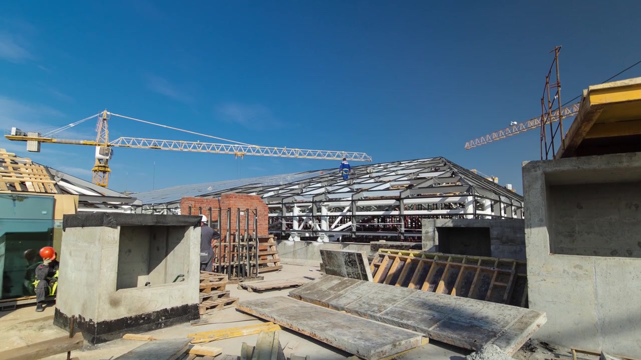 Builders and carpenters in uniform working on the roof timelapse. Construction site with yellow cranes of modern building. Blue cloudy sky on background view from rooftop
