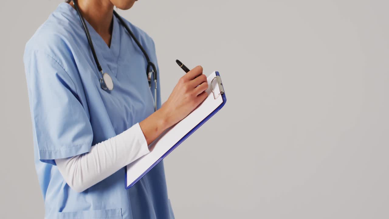 Video de una médica birracial escribiendo en un portapapeles sobre fondo azul