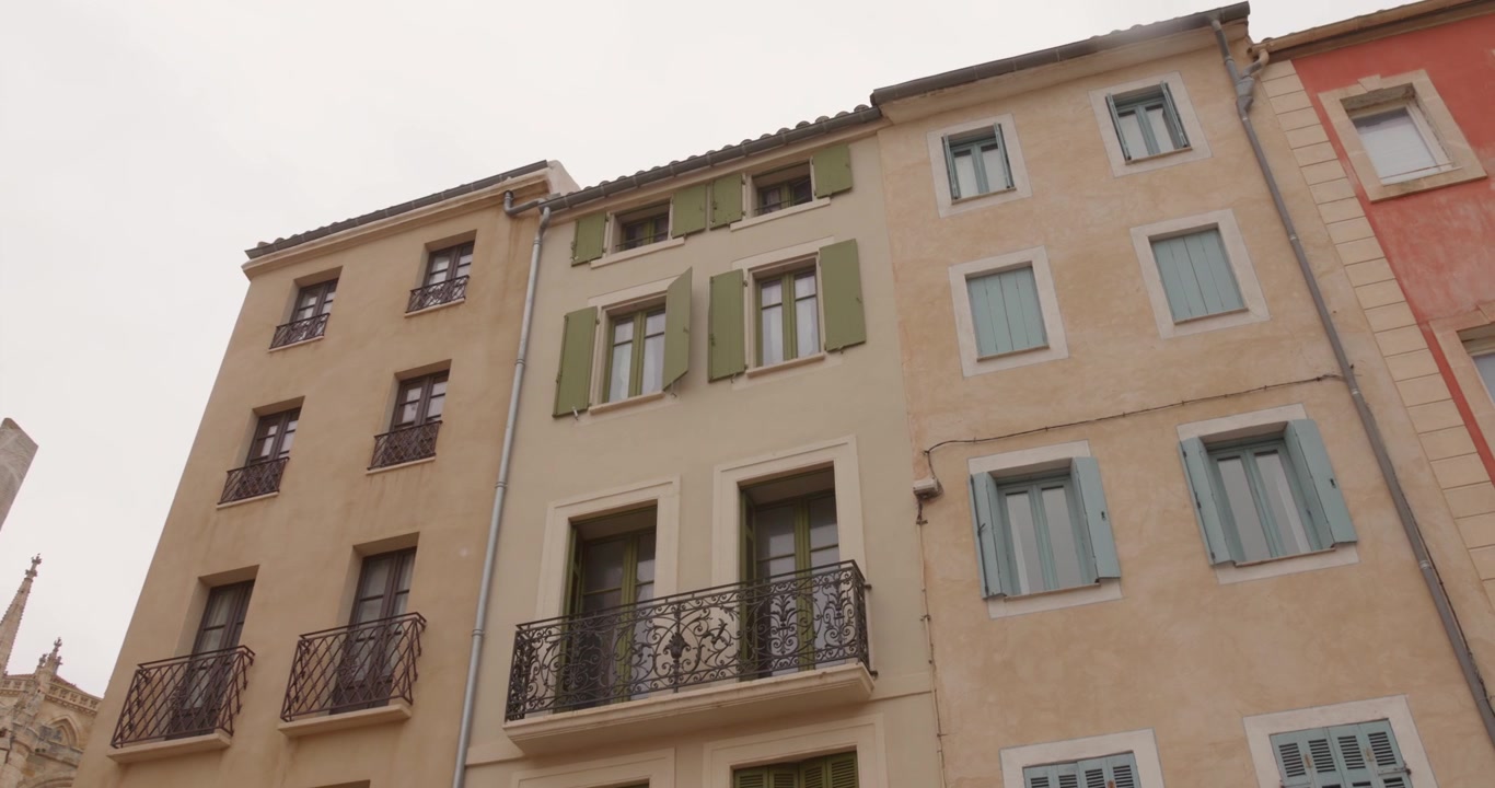 Vista de baixo para cima de edifícios de apartamentos franceses tradicionais com persianas coloridas na praça principal de Narbonne.