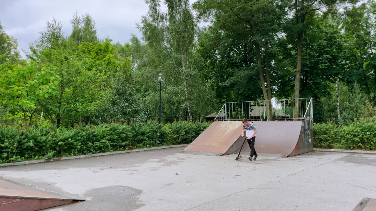 Slim boy riding his scooter on the skater's ground. Active sportive teenage having fun outdoors.