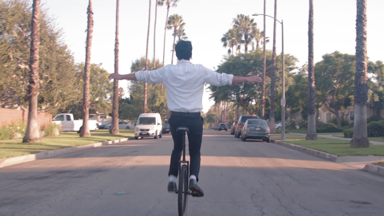 Man riding a unicycle down a palm tree lined street