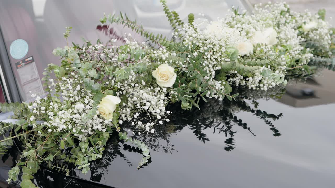 white roses and baby's breath flowers arranged on a black wedding car hood
