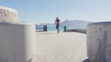 Video-of-caucasian-man-with-dreadlocks-skateboarding-on-sunny-beachside-promenade