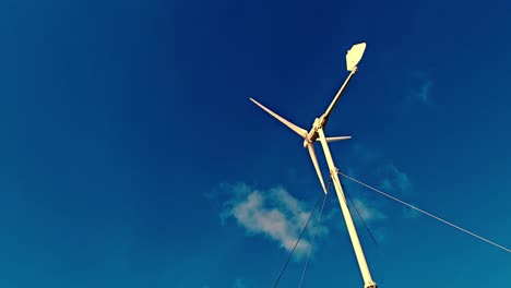 Small-white-wind-turbine-with-three-blades,-standing-in-front-of-a-clear-blue-sky