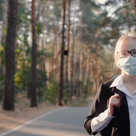 masked schoolboy walks down the road through park with tall trees