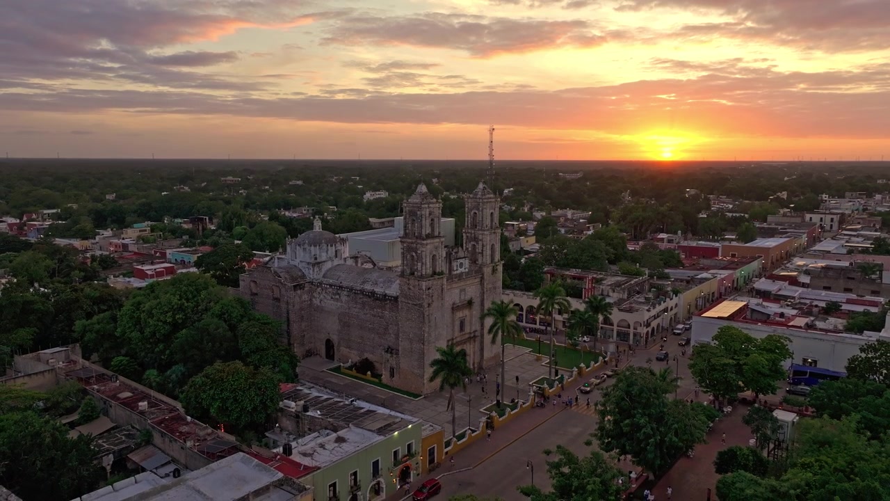 Vista aerea con drone sui tetti di Valladolid, Yucatan, Messico, al tramonto, con una calda luce ambrata che si diffonde sulla città coloniale verso l'orizzonte.
